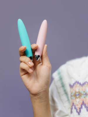 Close-up of a hand holding pink and blue vibrators against a purple background.